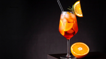 Aperol Spritz podany w kieliszku do wina z plasterkiem pomarańczy i rozmarynem.